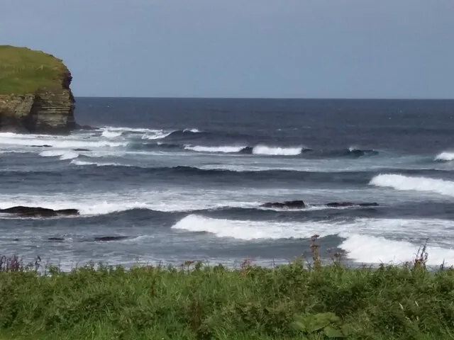 Ocean waves rolling towards a rocky shoreline on a cloudy day