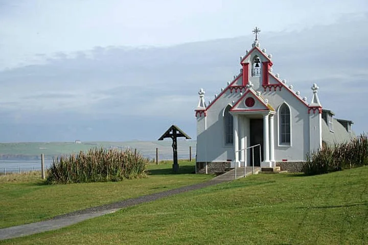 A small white chapel with red accents near a coastal shoreline