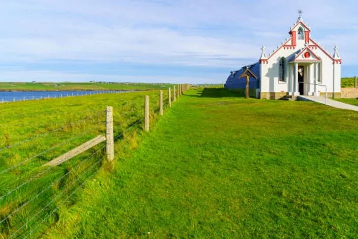 Small white chapel located in a bright green grassy field by the water